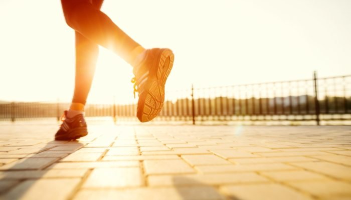 Runner feet running on road closeup on shoe. woman fitness sunrise jog workout welness concept.