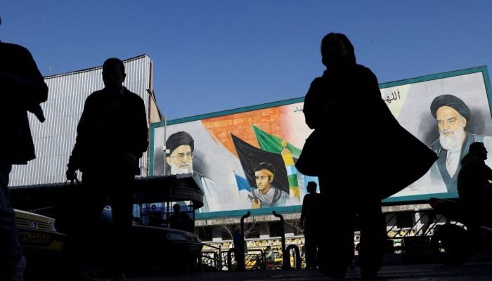 Pessoas caminham perto de um mural com imagens do líder supremo do Irã, o aiatolá Ali Khamenei...