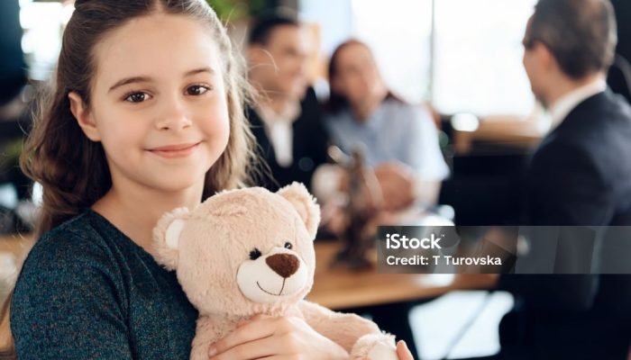 A young girl stands with a teddy bear and smiling at camera. Beautiful girl with parents stands in the office of a lawyer.